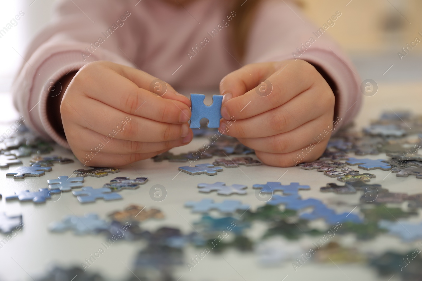 Photo of Little child playing with puzzles at table, closeup