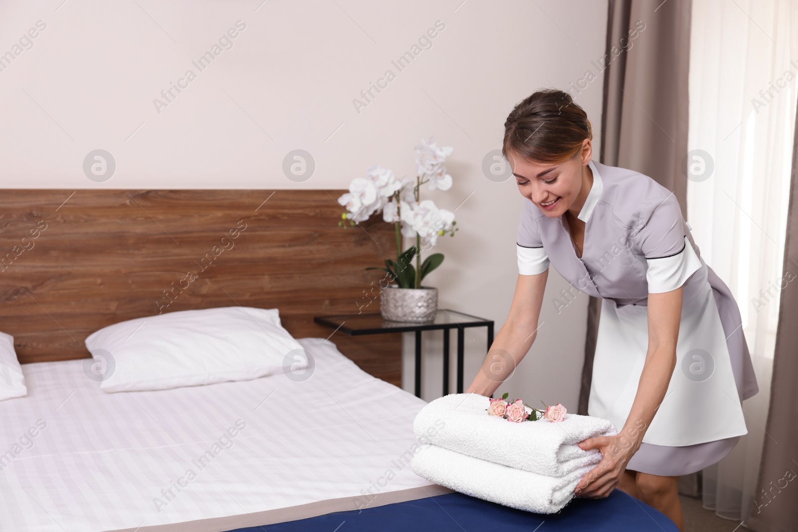 Photo of Beautiful chambermaid putting fresh towels on bed in hotel room