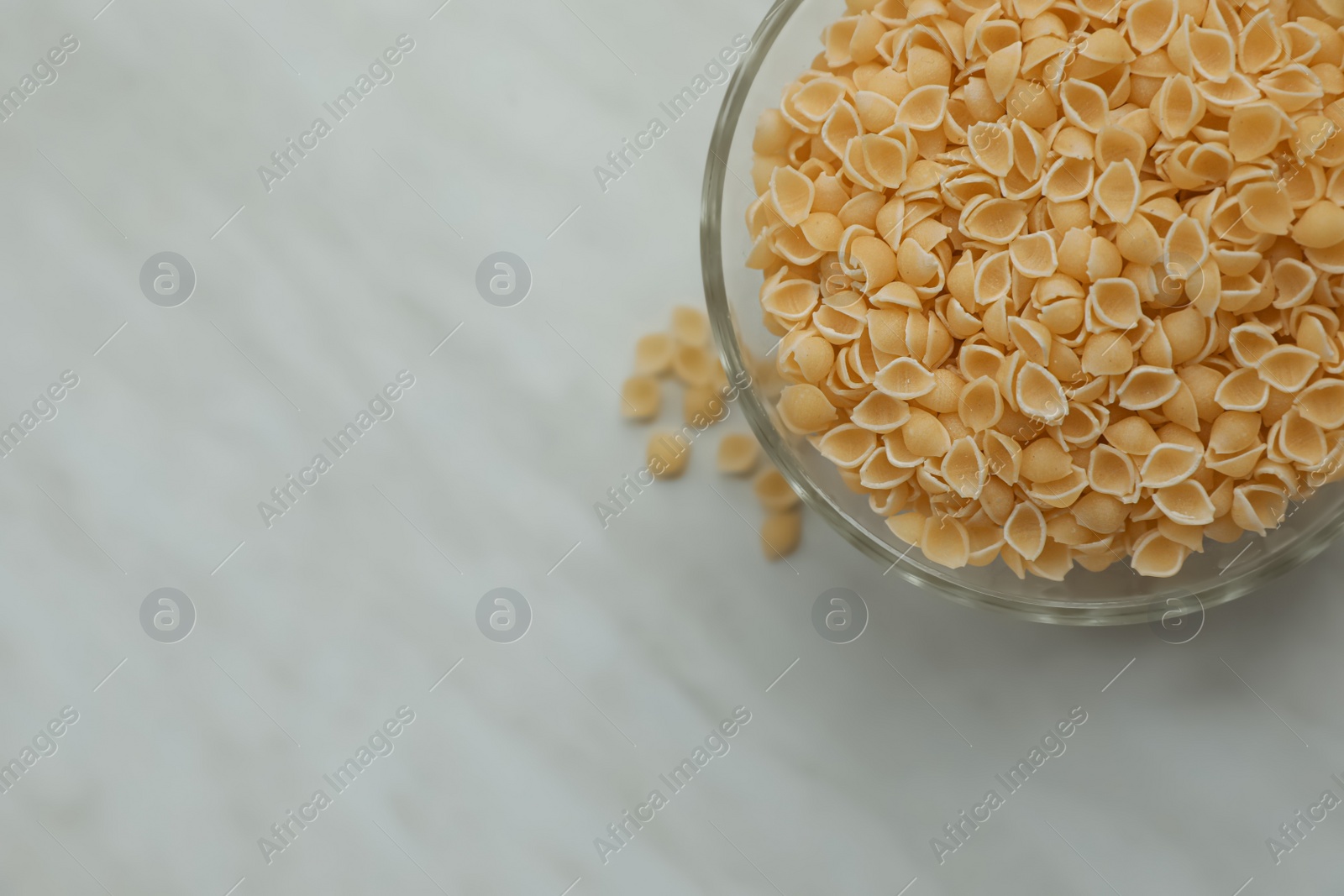 Photo of Bowl with uncooked conchiglie pasta on white marble table, flat lay. Space for text