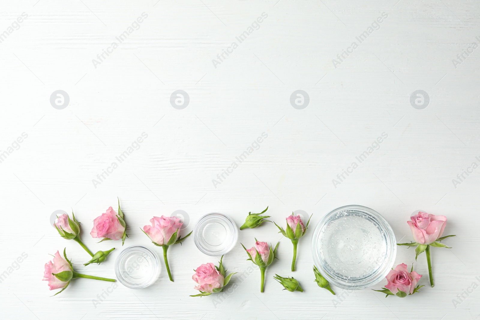 Photo of Flat lay composition with cosmetic gel and beautiful flowers on white wooden table. Space for text