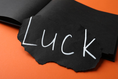 Photo of Sheet of paper and notebook with word LUCK on orange background, closeup