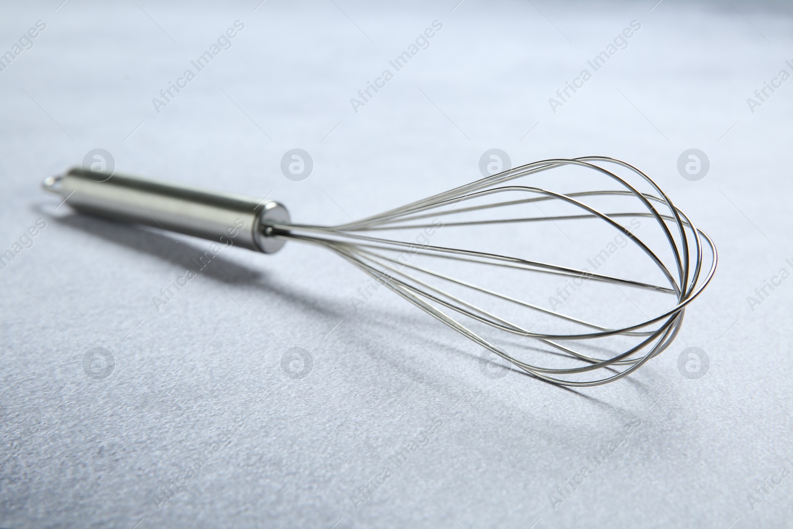 Photo of Metal whisk on gray table, closeup. Kitchen tool