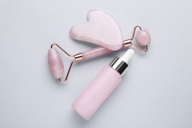 Gua sha stone, face roller and bottle of serum on light background, flat lay