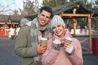 Photo of Happy couple in warm clothes with drinks at winter fair. Christmas season