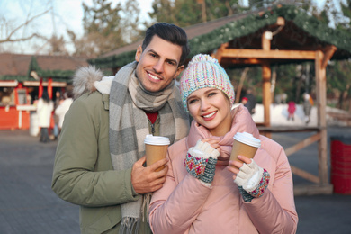 Happy couple in warm clothes with drinks at winter fair. Christmas season