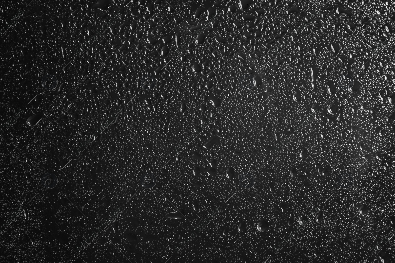 Photo of Glass with rain drops against dark background