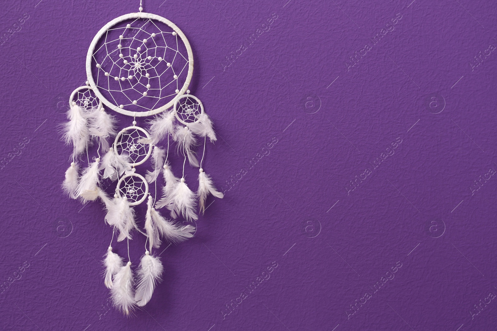 Photo of Beautiful handmade dream catcher on purple wall. Space for text