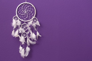 Photo of Beautiful handmade dream catcher on purple wall. Space for text