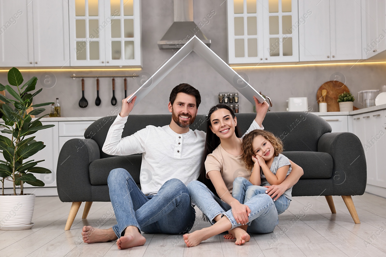 Photo of Housing concept. Happy husband holding plastic roof over his family while sitting on floor at home