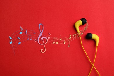 Staff with music notes and treble clef flowing from yellow earphones on red background, top view