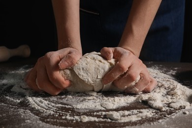 Photo of Making bread. Woman kneading dough at wooden table on dark background, closeup