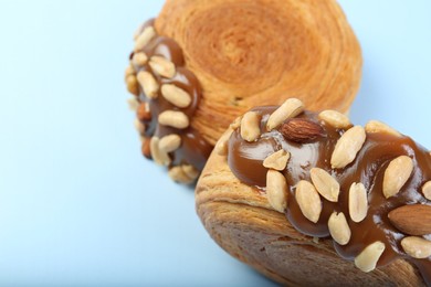 Photo of Tasty puff pastry. Supreme croissants with chocolate paste and nuts on light blue background, above view. Space for text