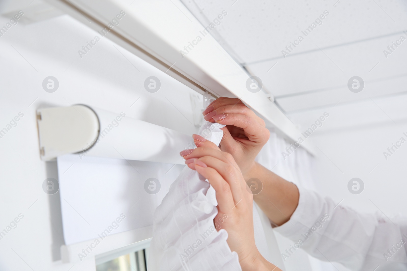 Photo of Woman hanging window curtain indoors, closeup. Interior decor element