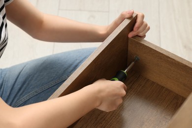 Photo of Woman with screwdriver assembling drawer indoors, closeup