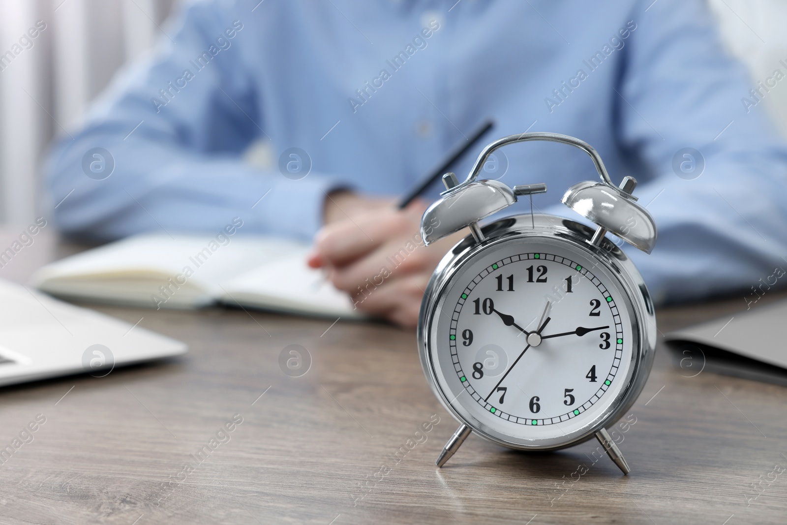 Photo of White alarm clock and man working at table, closeup. Space for text