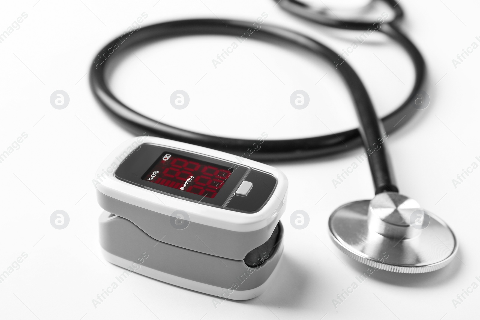 Photo of Modern fingertip pulse oximeter and stethoscope on white background, closeup