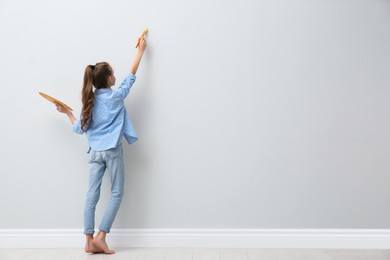 Little girl painting on light wall indoors, back view. Space for text