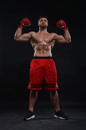 Photo of Man in boxing gloves celebrating victory on black background, low angle view