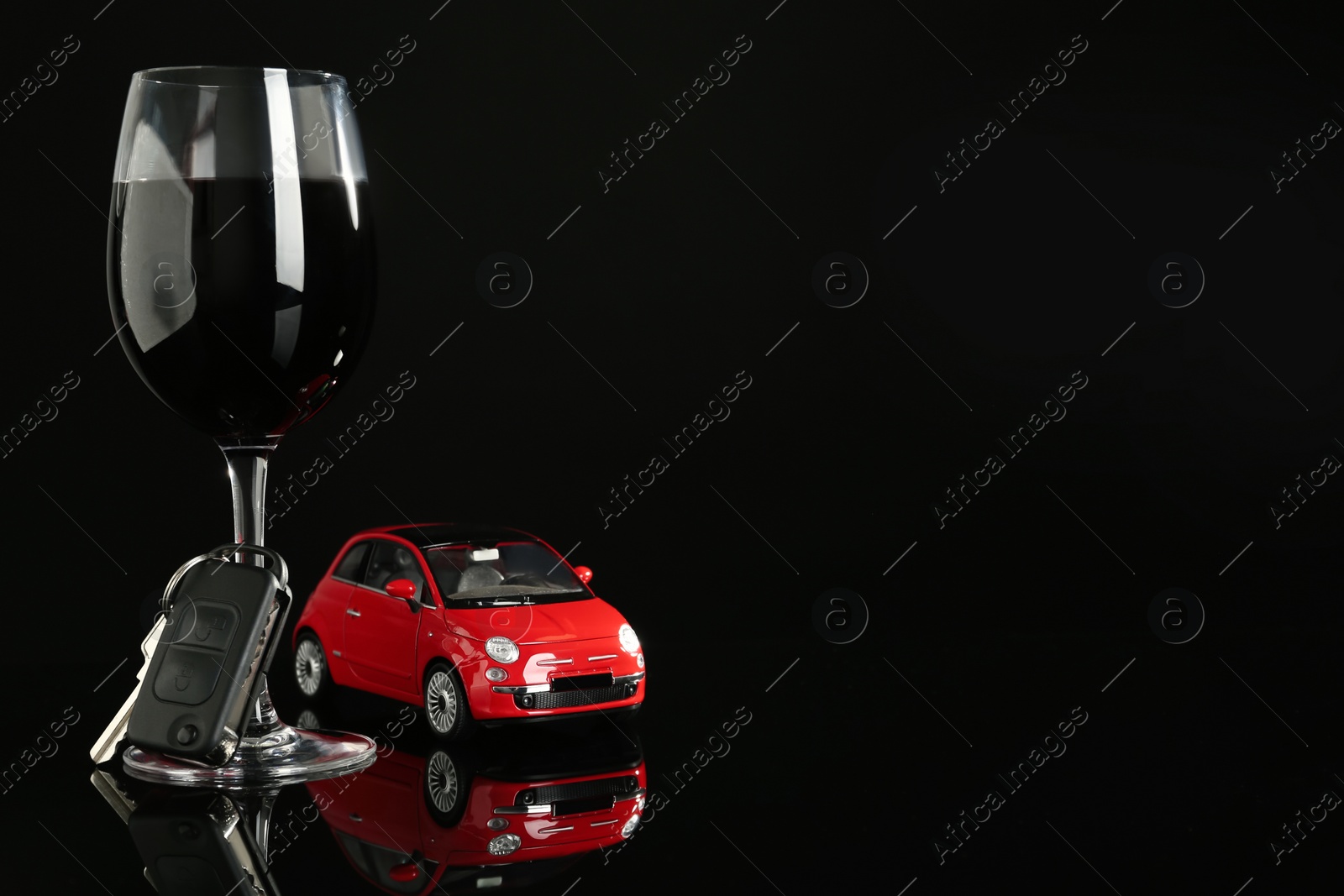 Photo of Car key, toy auto near glass of alcohol on black table, space for text. Dangerous drinking and driving