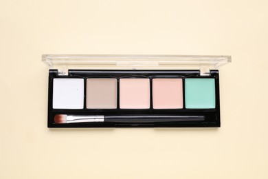 Colorful contouring palette with brush on beige background, top view. Professional cosmetic product