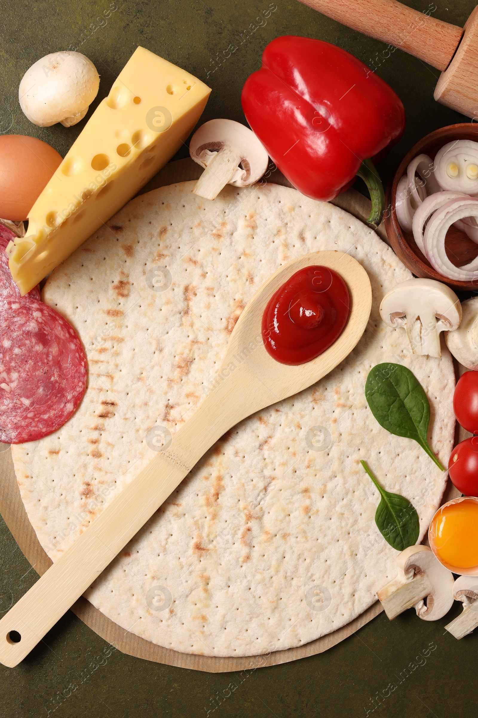 Photo of Pizza base, spoon with tomato sauce and products on green textured table, flat lay