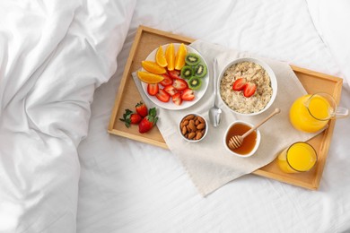 Photo of Tasty breakfast served in bed. Oatmeal, juice, fruits, almonds and honey on tray, top view