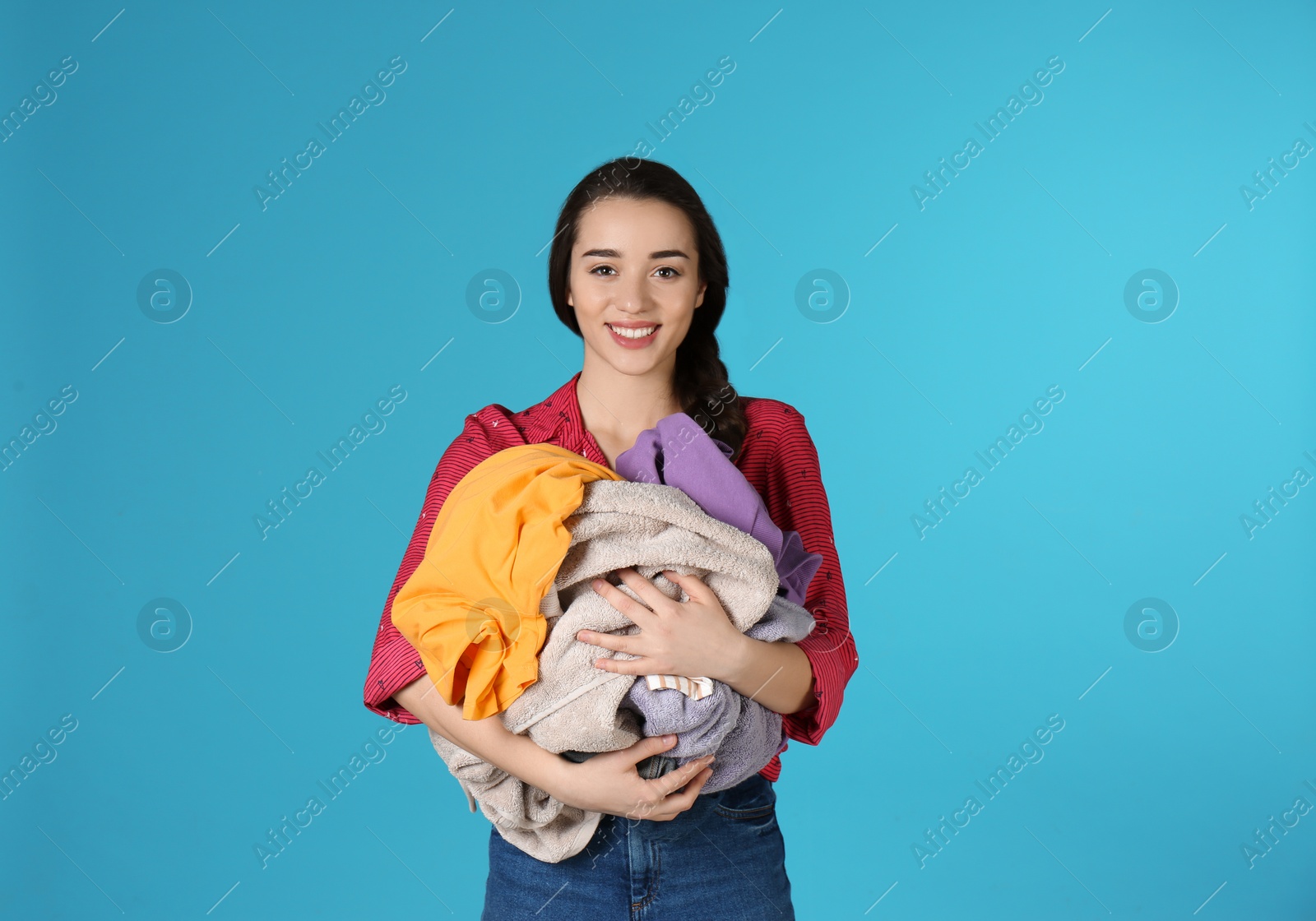 Photo of Happy young woman holding pile of dirty laundry on color background