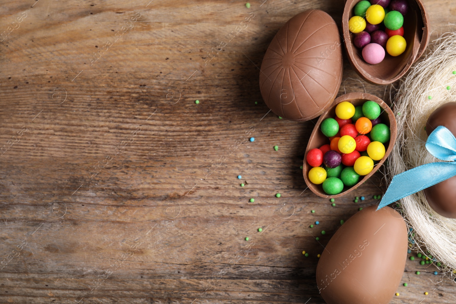 Photo of Tasty chocolate eggs with colorful candies on wooden table, flat lay. Space for text