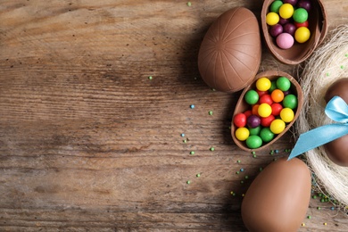 Tasty chocolate eggs with colorful candies on wooden table, flat lay. Space for text