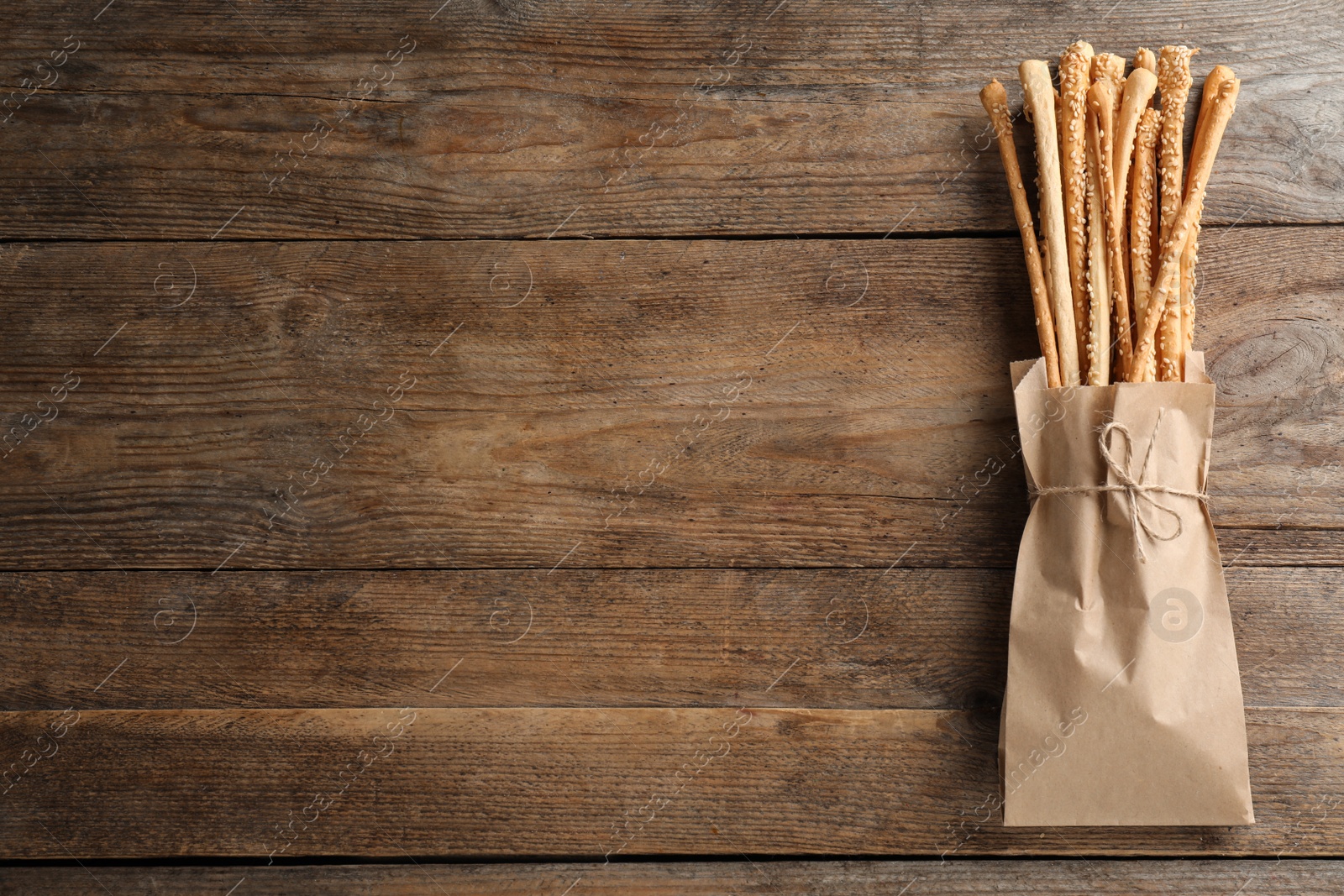 Photo of Delicious grissini sticks in paper bag on wooden table, top view. Space for text