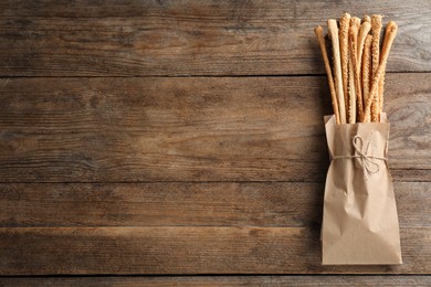 Photo of Delicious grissini sticks in paper bag on wooden table, top view. Space for text