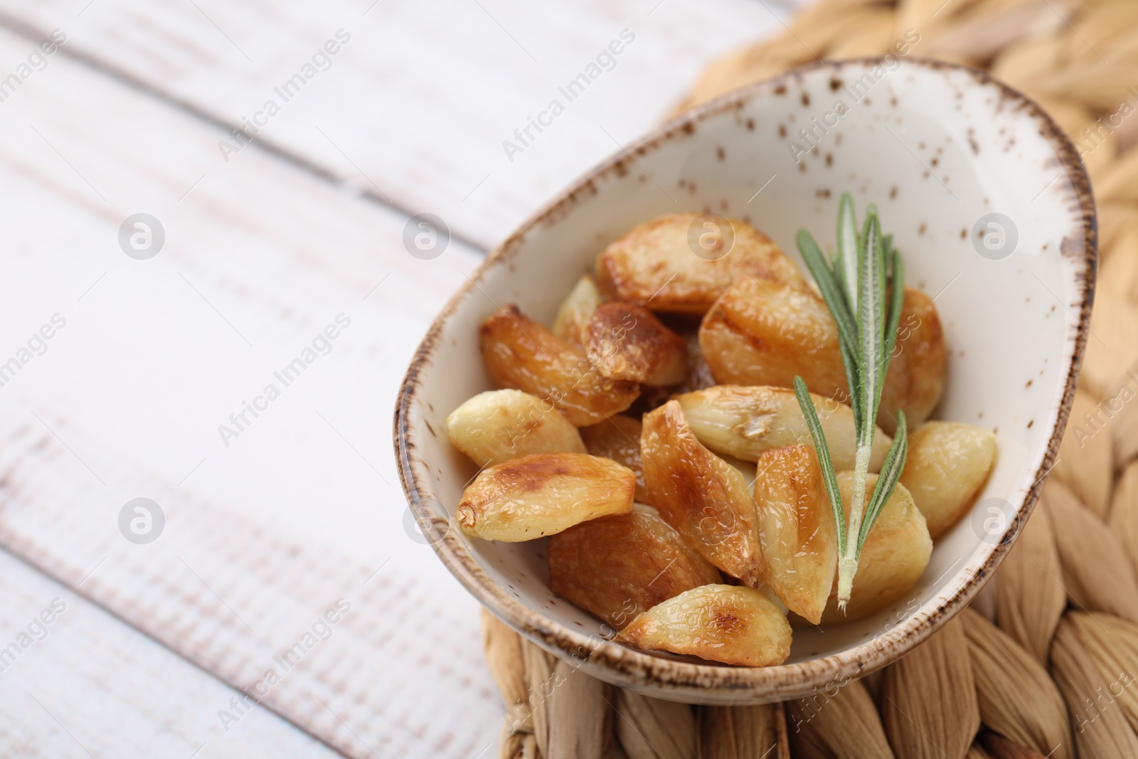 Photo of Fried garlic cloves and rosemary on white wooden table, closeup. Space for text