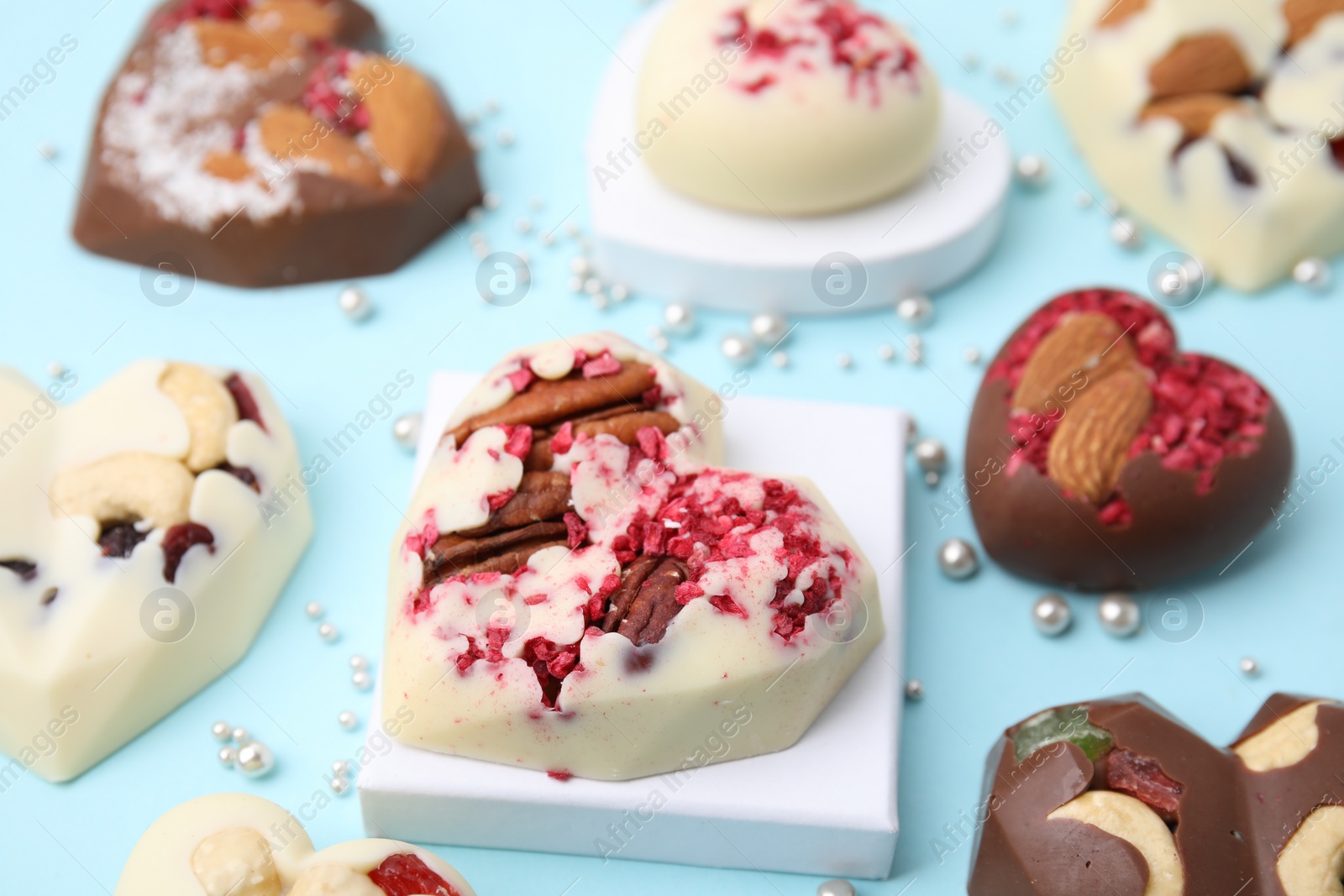 Photo of Tasty chocolate heart shaped candies with nuts on light blue background