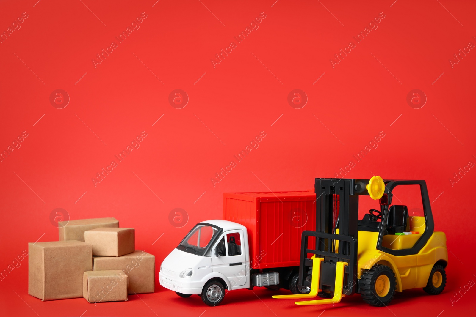 Photo of Different toy vehicles with boxes on red background. Logistics and wholesale concept