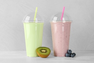 Plastic cups of different tasty smoothie and fresh fruits on white wooden table