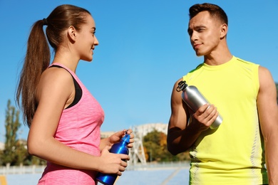 Photo of Young sporty couple holding bottles of water at stadium on sunny day