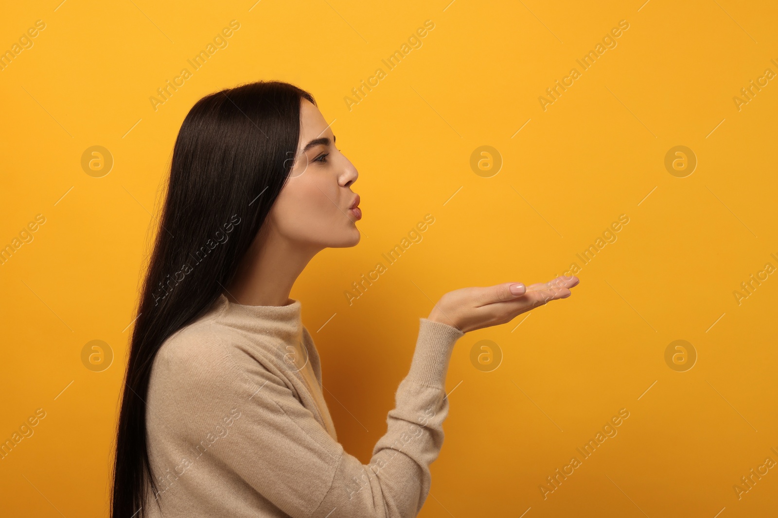 Photo of Beautiful young woman blowing kiss on orange background. Space for text