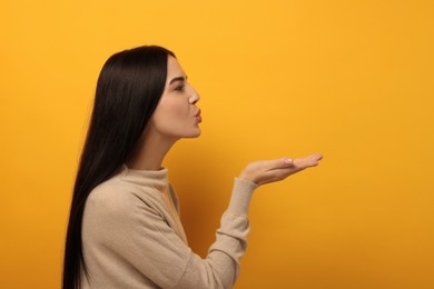 Photo of Beautiful young woman blowing kiss on orange background. Space for text