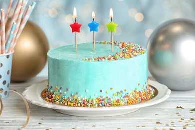 Fresh delicious cake with candles on table against blurred lights