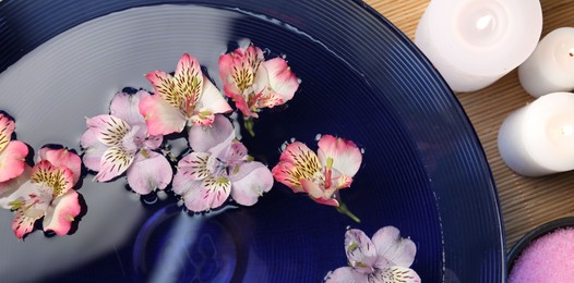 Bowl of water with flowers, candles and sea salt on table, top view. Spa treatment