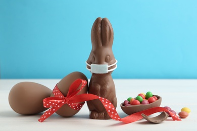 Chocolate bunny with protective mask and eggs on white wooden table. Easter holiday during COVID-19 quarantine