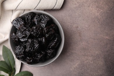 Photo of Sweet dried prunes in bowl on light brown table, top view. Space for text