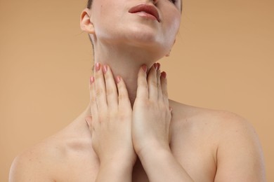 Woman touching her neck on beige background, closeup