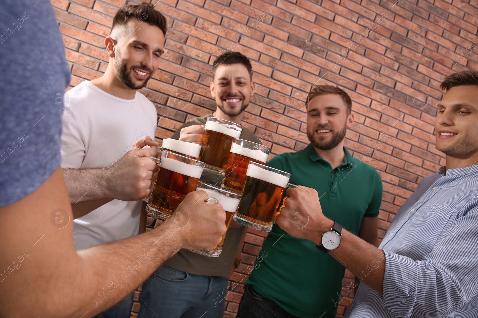 Photo of Friends clinking glasses of beer near red brick wall