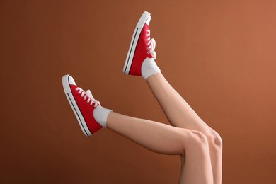 Photo of Woman wearing red classic old school sneakers on brown background, closeup