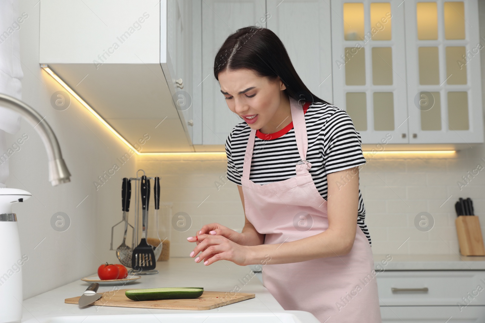 Photo of Young woman cutting finger with knife while cooking in kitchen