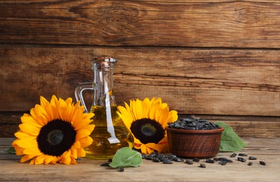 Photo of Sunflower cooking oil, seeds and yellow flowers on wooden table