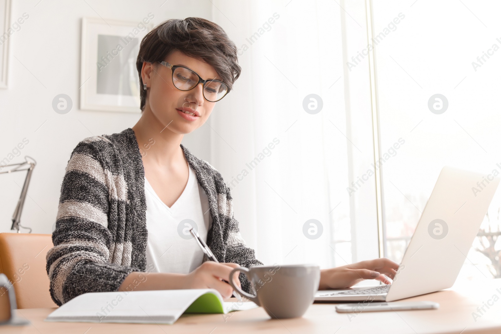 Photo of Young woman working with laptop at desk. Home office