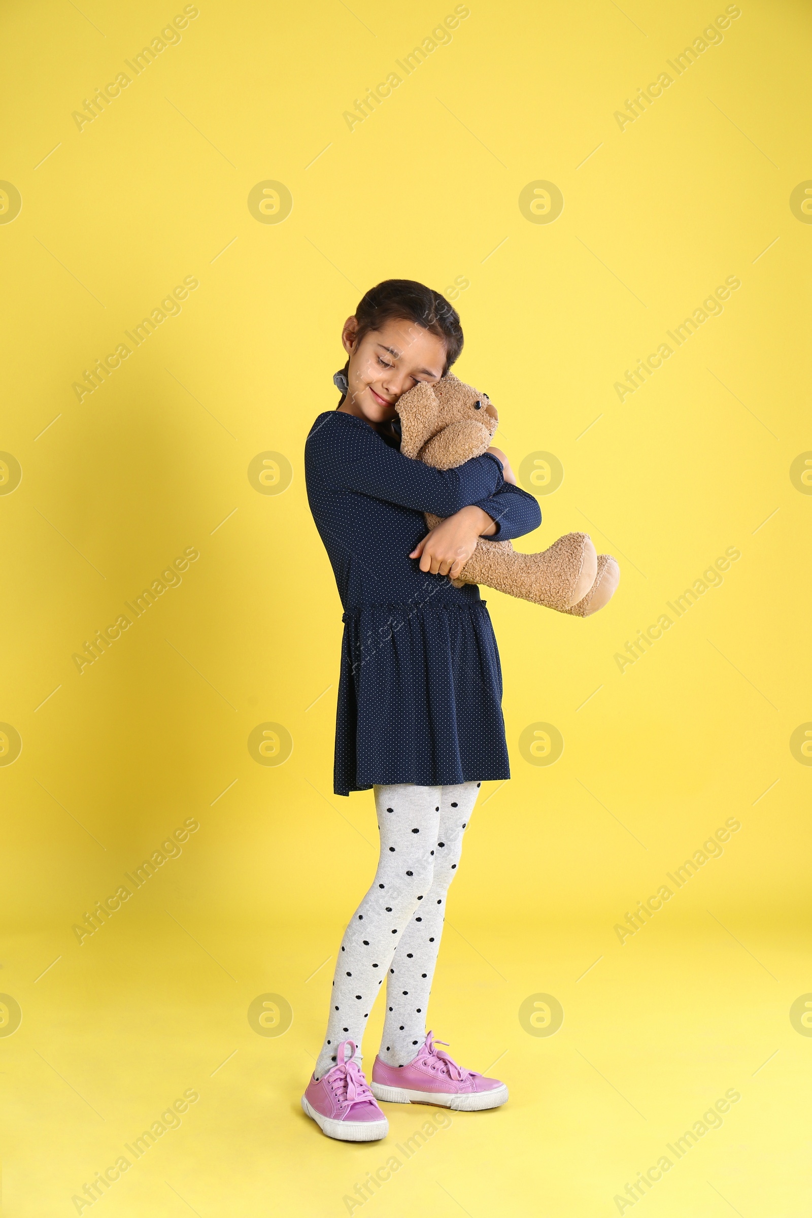 Photo of Cute little girl with toy bunny on yellow background