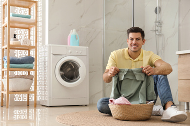 Photo of Man with clean clothes near washing machine in bathroom. Laundry day